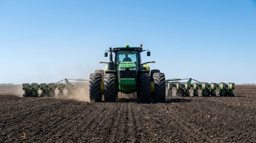 A large 4WD tractor with dual agricultural wheels on both axles pulling a wide planter across a field.