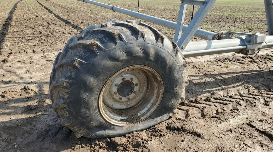 A close-up of an underinflated irrigation tire showing sidewall bulge.