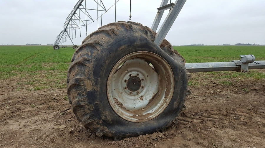 A close-up of an irrigation tire with a slightly deflated appearance, showing the sidewall flexing under the weight of the pivot.